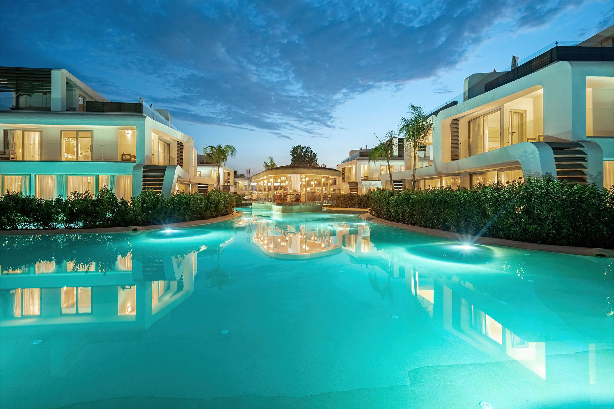 Club Arona villas at dusk, lit windows reflected in the property's shared turquoise water