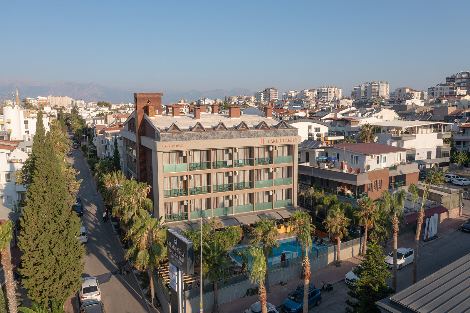 Laren Family Hotel in evening light on a palm-lined Lara street, its courtyard pool beside the building
