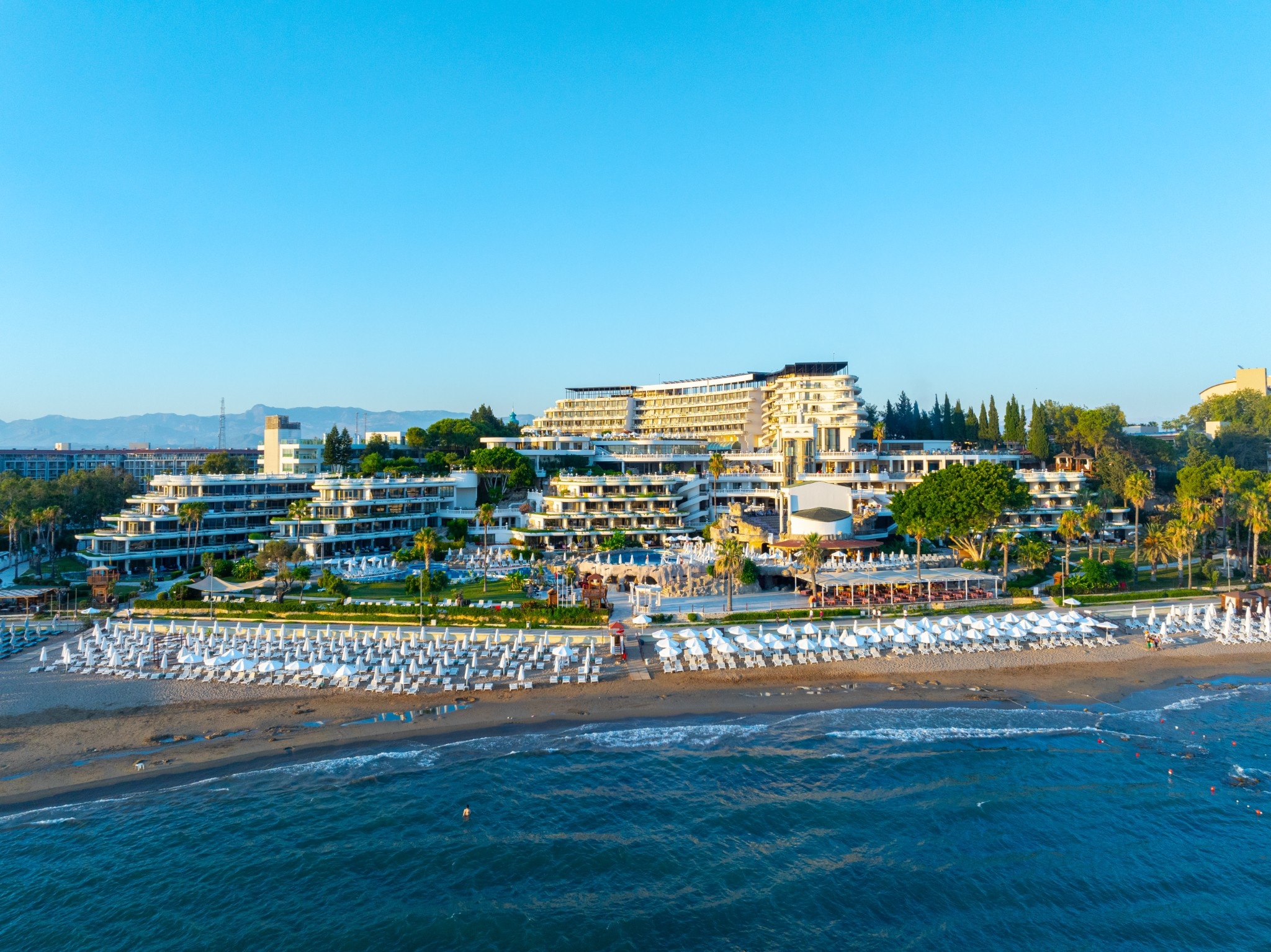 Sunrise Queen seen from the sea: terraced resort buildings behind a beach lined with white parasols